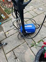 Front view of blue Simoniz pressure washer placed on stone pavement with attached black hose and power cord coiled around.