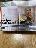Box of acrylic recipe book holder with a cookbook partially open displayed within the holder.