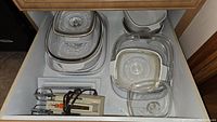 Photo showing assortment of Pyrex and Corningware bakeware dishes and lids in a drawer.