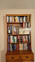 Photo of full bookshelf with arranged books on four shelves and wooden bookshelf with drawers.