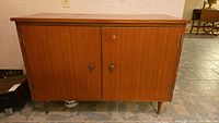 Front view of vintage wooden storage cabinet with two doors, brass hinges, round wooden knobs, and tapered legs.