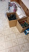 Two cardboard boxes containing assorted Christmas lights of various types and colors, holiday wreath wrapped in plastic visible in background.