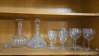 Two crystal decanters and several wine glasses arranged on a wooden shelf.