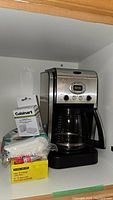 Cuisinart 14-cup coffee maker with digital display, glass carafe, charcoal water filters, and cone coffee filters placed on shelf.