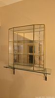 Large brass-framed glass display case with multiple shelves, wall-mounted on glass bracket.