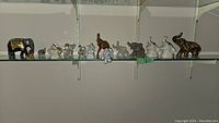 Overview of all elephant figurines displayed on glass shelves including large decorated black elephant, clear glass elephants, white ceramic elephants, and other small figurines.
