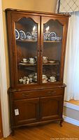 Full view of the corner cabinet showing two glass doors with shelves inside and wooden storage below.