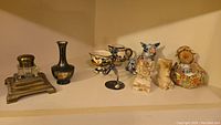 Wide shot of all items arranged on a shelf, showing ink well, vase, creamer, sugar bowl, bolt man figurine, onyx bookends, and fabric doll with candle holder