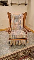 Front view of wooden colonial style rocking chair with multicolor cushioned seat, back, and bottom skirt.