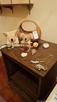 Photo of all items on wooden shelf: wicker basket, two plush bears, two necklaces, six small decorative items including smiley face stone, owl figurine, and carvings.