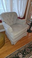 Front angled view of vintage cloth covered swivel rocker recliner chair showing tufted backrest, cushioned armrests, and skirted base on hardwood floor.