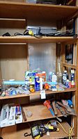 Shelf with assorted hand tools, lubricants, and accessories including WD-40, small tools, and protective glasses.