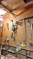 Wide view of wooden pegboard with assorted hand tools including wrenches, screwdrivers, level, LiteDriver, and putty knives hung for display.