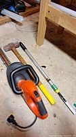 Full view showing Black & Decker hedge trimmer, Lee Valley weed scraper, and sledge hammer on concrete floor with wooden bench nearby.