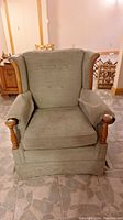 Front view of a vintage casual chair with green fabric upholstery and prominent wooden accents on wings and arm ends.