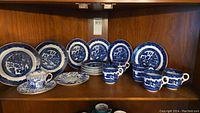 Wide shot of vintage blue and white cups, saucers, and plates on wooden shelf showing full set