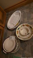 Stacked vintage serving platters and bowls displayed on the floor showing a variety of styles including floral patterns and ribbed designs