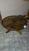 Full view of the round wagon wheel coffee table with smokey glass top on a tiled floor.