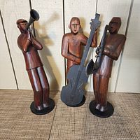 Front angle view of the three wooden musician figures placed side by side showing trumpet, bass, and saxophone players.