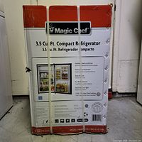 Front of box showing Magic Chef branding, 3.5 cu ft compact refrigerator text and product image, strapped with plastic bands
