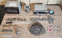 Complete lot including two car stereos, Mercedes-Benz trinket bowl or ashtray, various car emblems and badges spread on a textured surface