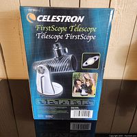 Front side of the original box showing Celestron FirstScope Telescope branding, image of the telescope, and celestial images.