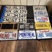 Top down view of assorted license plates, including foreign and souvenir plates, and two brass frames