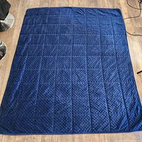 Top view of blue weighted blanket laid out flat on a wooden floor, showing textured side with grid of small raised dots.