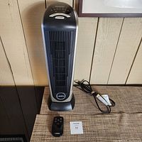 Front view of Lasko ceramic tower heater with power cord and remote control on the table.