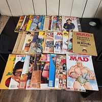 Top-down photo of 30+ vintage MAD magazines spread on floor with various cover arts visible including special issue covers such as 100th issue and Our 400th Monok issue.