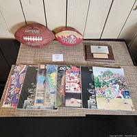 Full lot view showing the footballs, Arco Arena floor piece, and several yearbooks and sports magazines laid out on table.