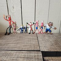 Front view of seven vintage PVC bendy figurines displayed on wooden floor against white panel wall.