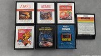 Seven Atari 2600 game cartridges including Vanguard, E.T., Dig Dug, Atlantis, Crystal Castles, Slot Racers, and Oink! arranged on a gray surface.