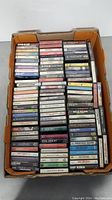 Top view of an open cardboard box filled with five vertical columns of cassette tapes, showing a large variety of artists and album titles.