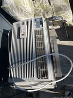 Front top view of white window air conditioner showing air vent, louvers, control panel with buttons, and included remote control on top.