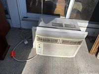View of the front and top of the white window air conditioner unit showing vents, control buttons, and power cord