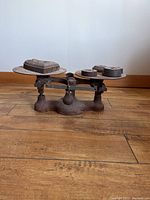 Side view of antique cast iron balance weigh scale, showing weighing plates with weights, base, and overall structure.