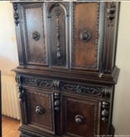 Front view of dark wood carved dining room storage chest, showing four cabinet doors with ornamental knobs and detailed wood carvings