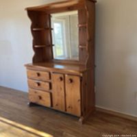 Front view of wooden dresser with attached mirror and side shelves, showing three drawers and two cabinets below.