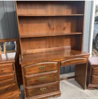 Medium-toned wooden dresser with three drawers on bottom and two shelves on top against a dark wall background.