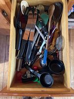Drawer containing various cooking utensils including spatulas, whisks, knives, and can opener