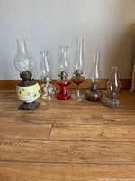 Group photo of six vintage oil lamps on wooden floor showing variety of bases and glass chimneys