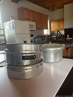 Aluminum double boiler parts stacked, showing two round pots of similar size.