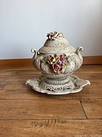 Front view of the closed ceramic serving dish with lid, showing ornate floral decorations and curved handles.