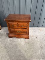 Front view showing three drawers and brass handles, wood finish with some wear.