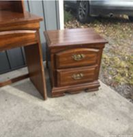 Side table standing outside showing full front and right side with its two drawers and brass handles.