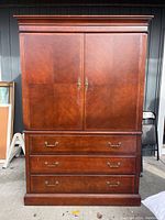 Closed front view of wooden TV armoire with paneled doors and three drawers below