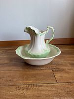 Side view of the wash pitcher placed inside the matching wash bowl on wood flooring against a plain wall.