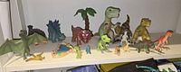 Full display shelf photo showing the dinosaur toys grouped together including the larger and smaller figures, and some accessories like a palm tree.