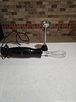 Immersion blender motor unit lying on countertop with blending shaft detached and wire whisk attachment visible next to motor unit